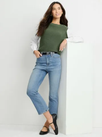 Woman wearing a white shirt under a green sweater-vest, cropped blue jeans and black ballet flats.