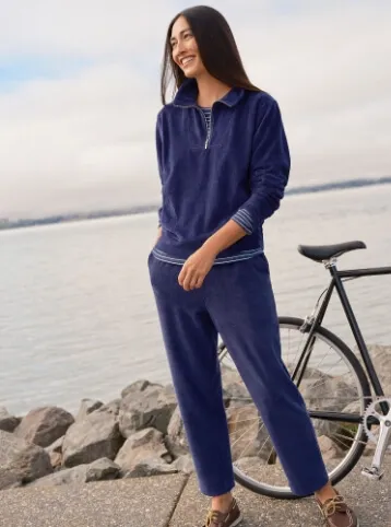 Woman wearing a navy blue sweatsuit; standing on a breakwater.