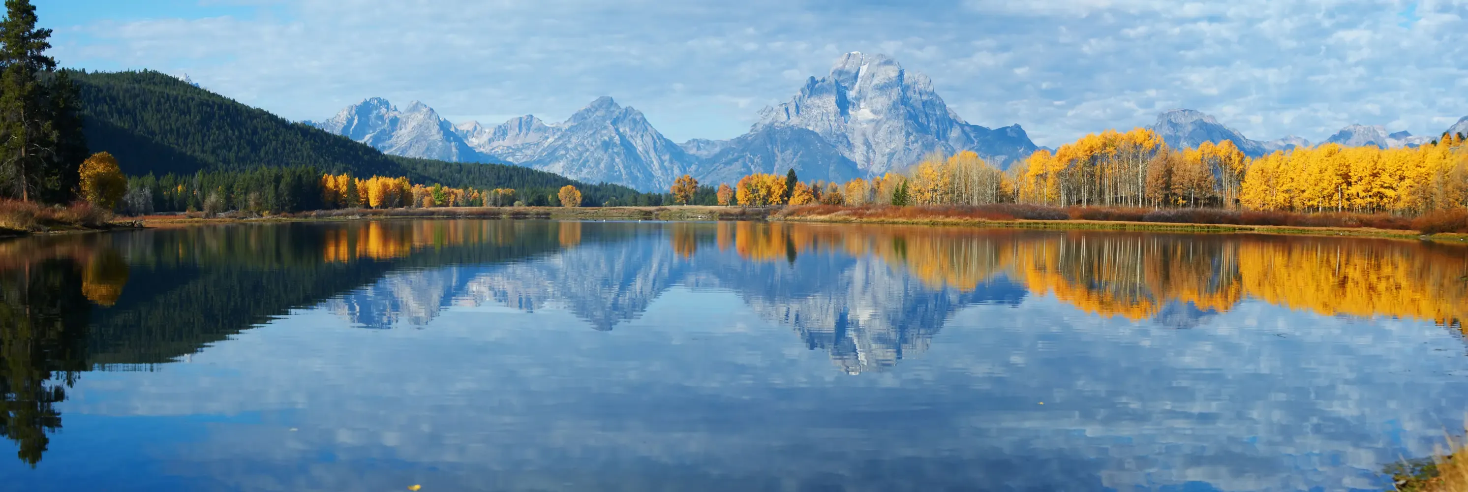 Snowy peaks and golden trees mirrored on a calm lake.