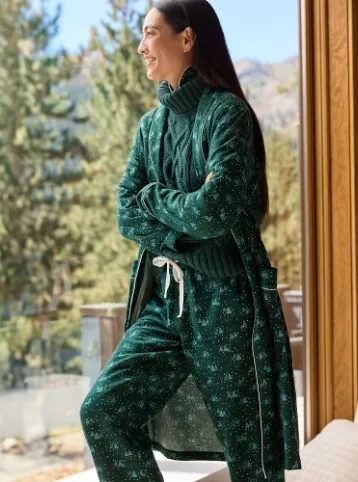 Woman wearing a green cable knit turtleneck sweater and matching green robe and pajama pants. 