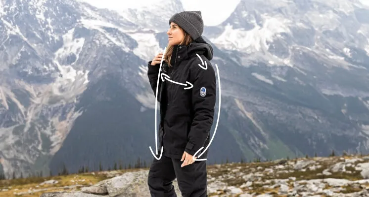Woman wearing a black squall jacket and gray stocking cap, standing in a snowy mountain landscape; white lines are drawn to indicate jacket measurements.