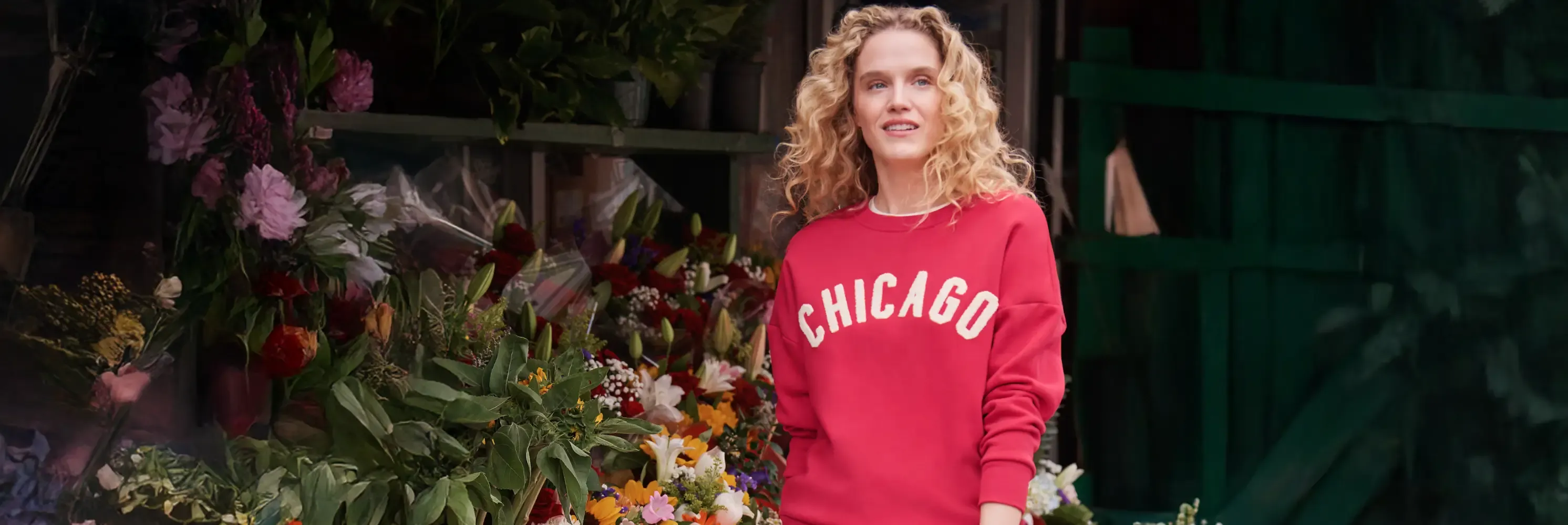 Blonde curly-haired woman in red Chicago sweatshirt at flower stand.