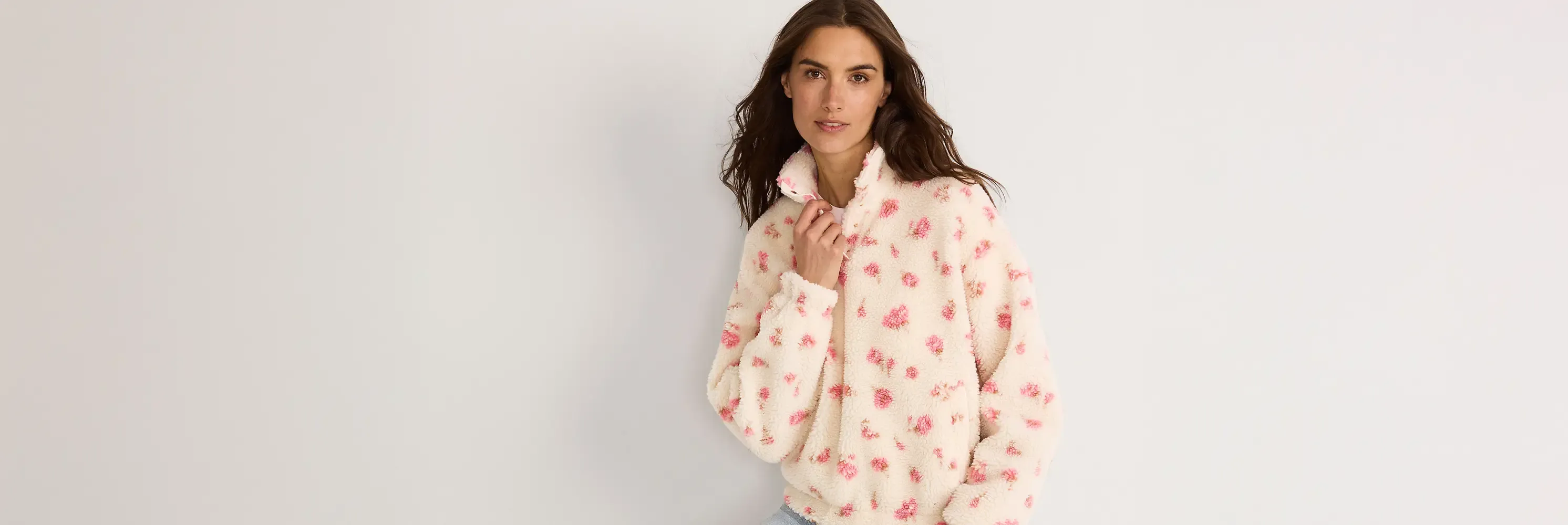 Brunette woman wearing cream sherpa pullover with pink floral pattern.