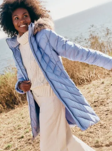 Woman wearing a blue, down insulated parka over a white cable knit turtleneck sweater.