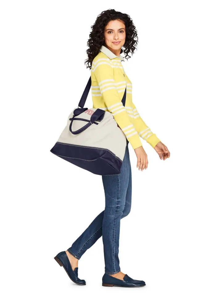 Woman wearing a yellow and white striped rugby shirt and blue jeans, carrying a white tote bag with navy blue trim. 