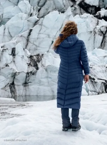 Woman wearing a long, blue Wanderweight insultated packable maxi coat.
