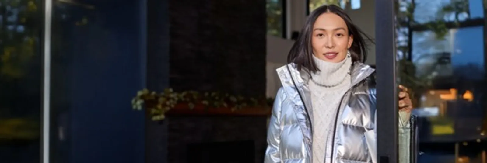 Woman wearing a white cable knit turtleneck sweater under a silver puffer jacket.