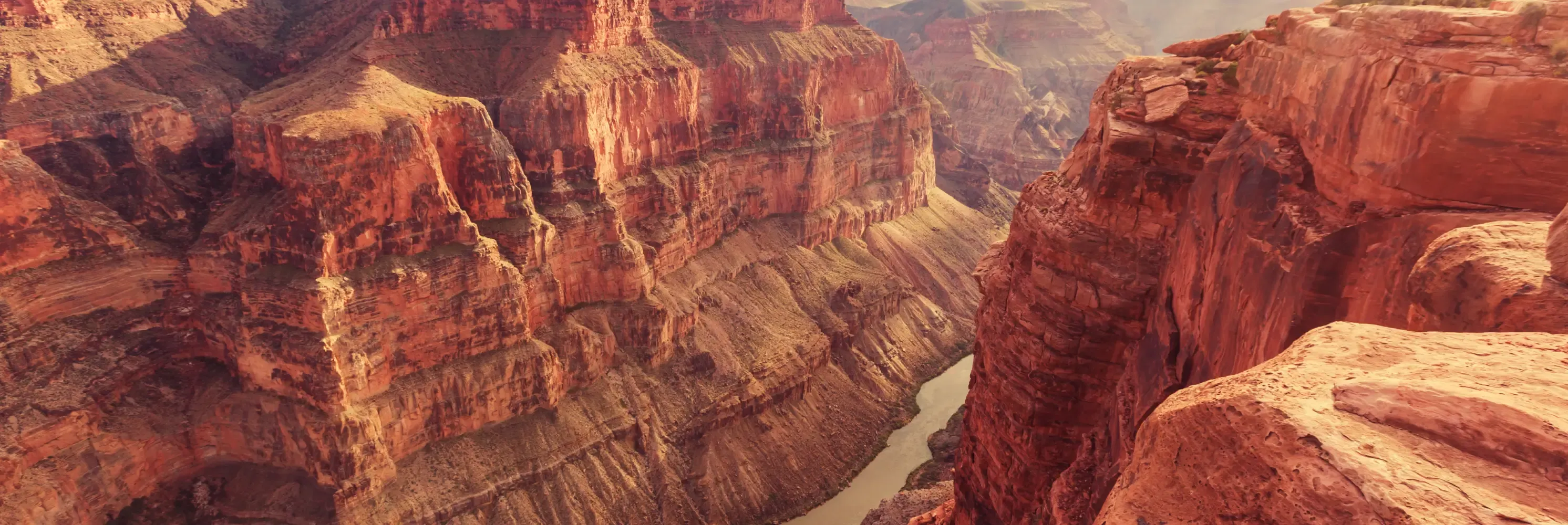 Sunlit red canyon walls with a river far below.