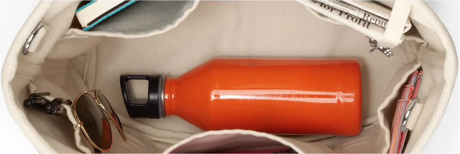 Open canvas bag showing a pair of sunglasses, books, a newspaper, and an orange water bottle inside.