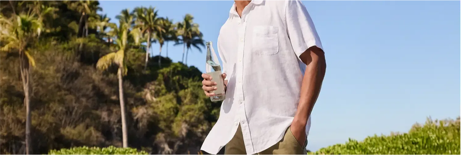 Man in a white short-sleeve button-up shirt and khaki shorts holding a glass bottle