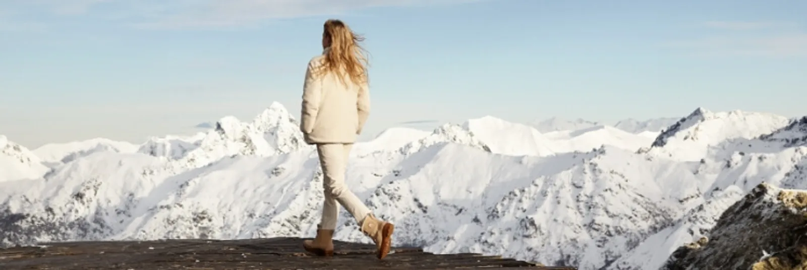 Woman wearing white winter outerwear and snow boots, walking in a snowy mountain landscape.