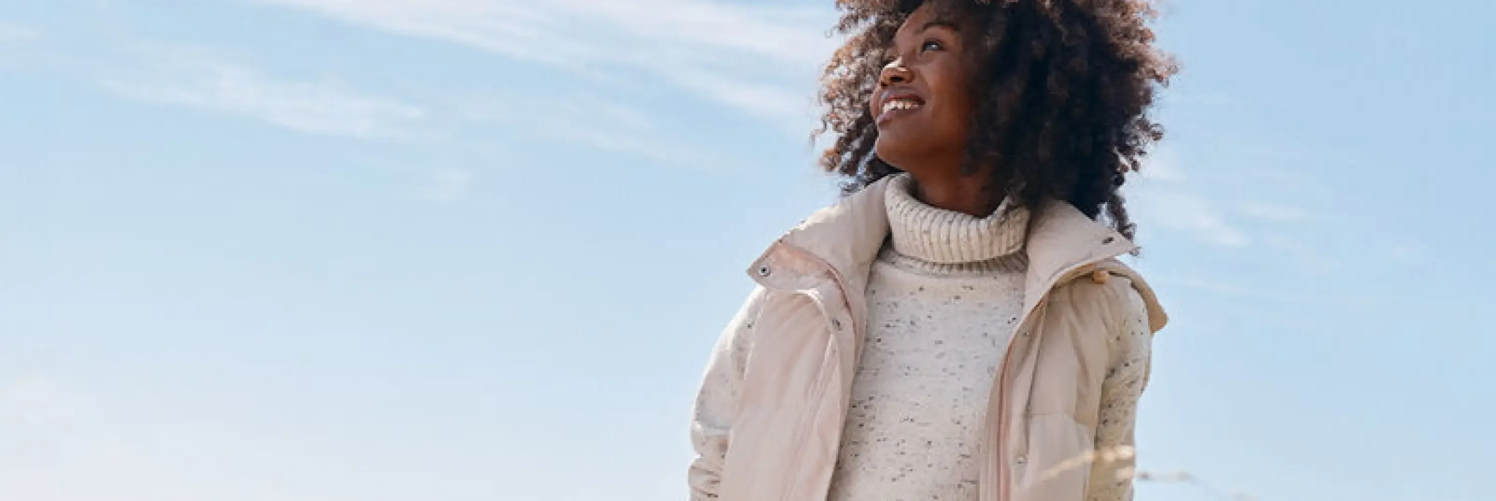 Woman with curly hair in beige jacket over speckled turtleneck sweater.