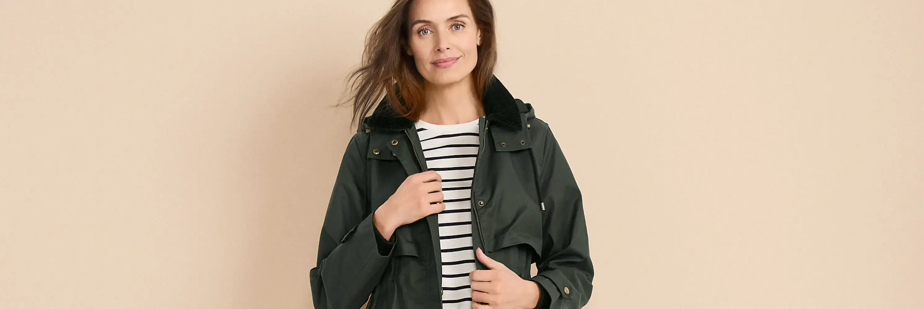 Woman in a dark green hooded utility jacket over a black and white striped shirt.