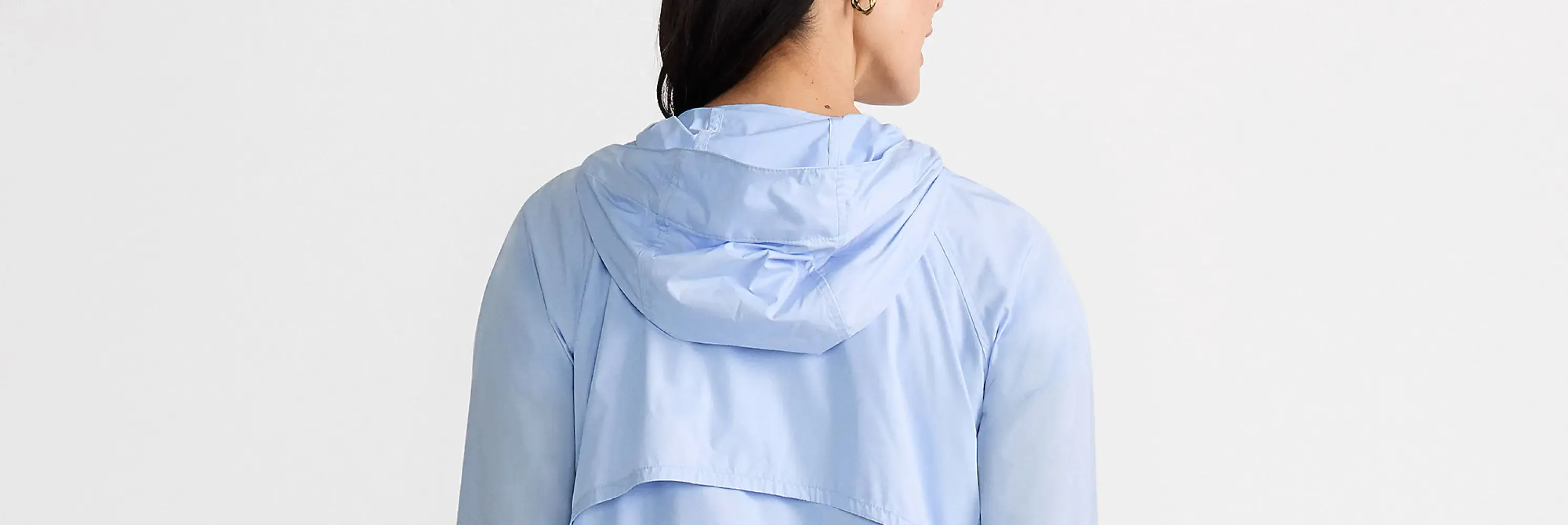 Woman in a light blue hooded rain jacket shown from behind.