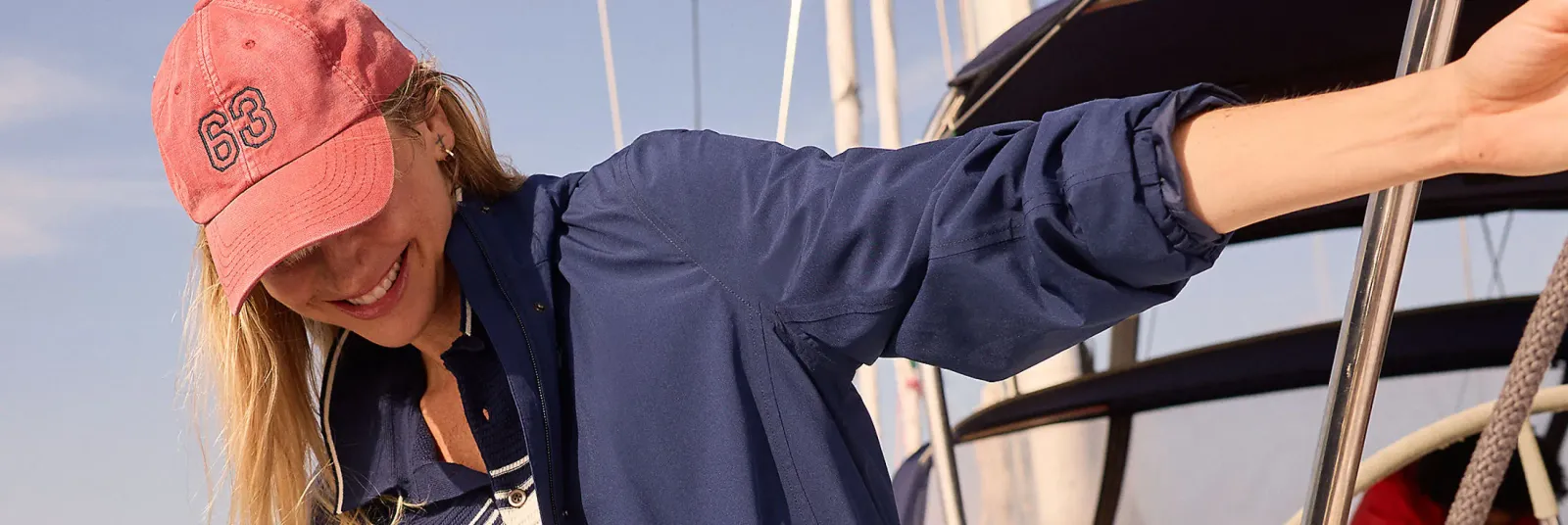 Woman in a navy windbreaker and coral cap on a sailboat.