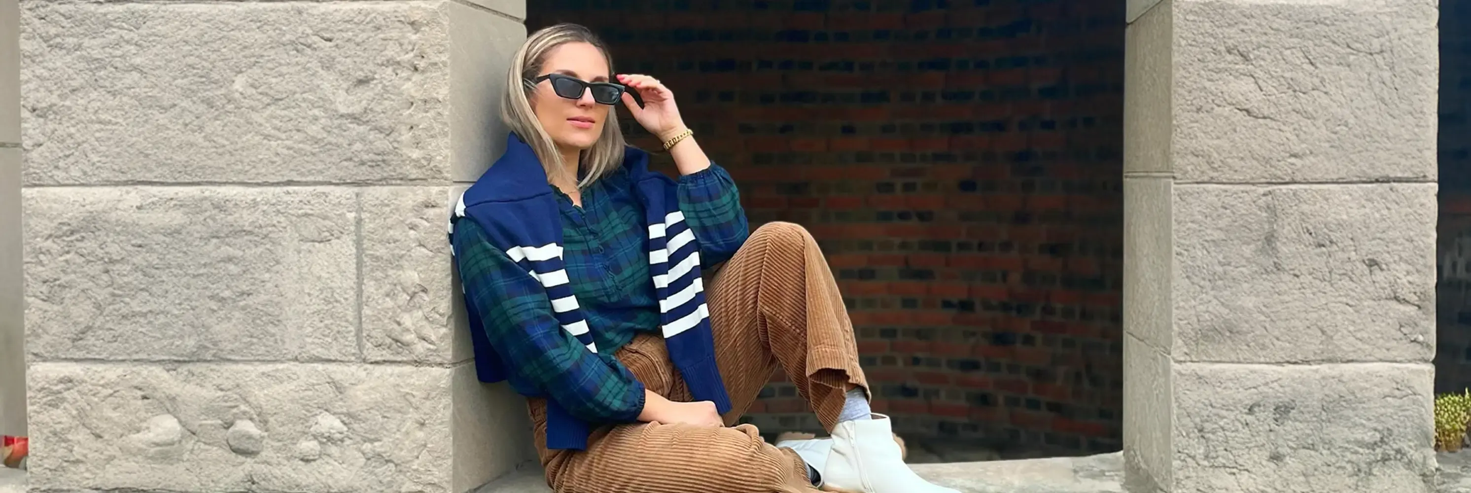 Woman wearing blue and green plaid shirt and brown corduroy pants, a blue and white striped sweater hung over her shoulders.