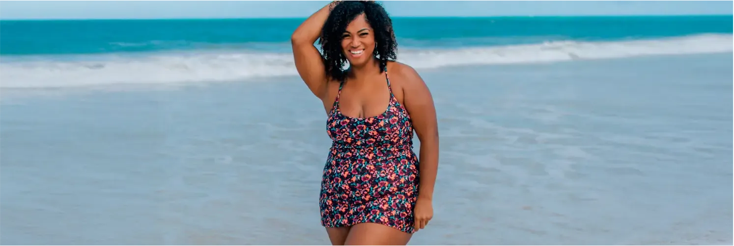 Woman wearing a plus size floral swim dress, walking on a beach.