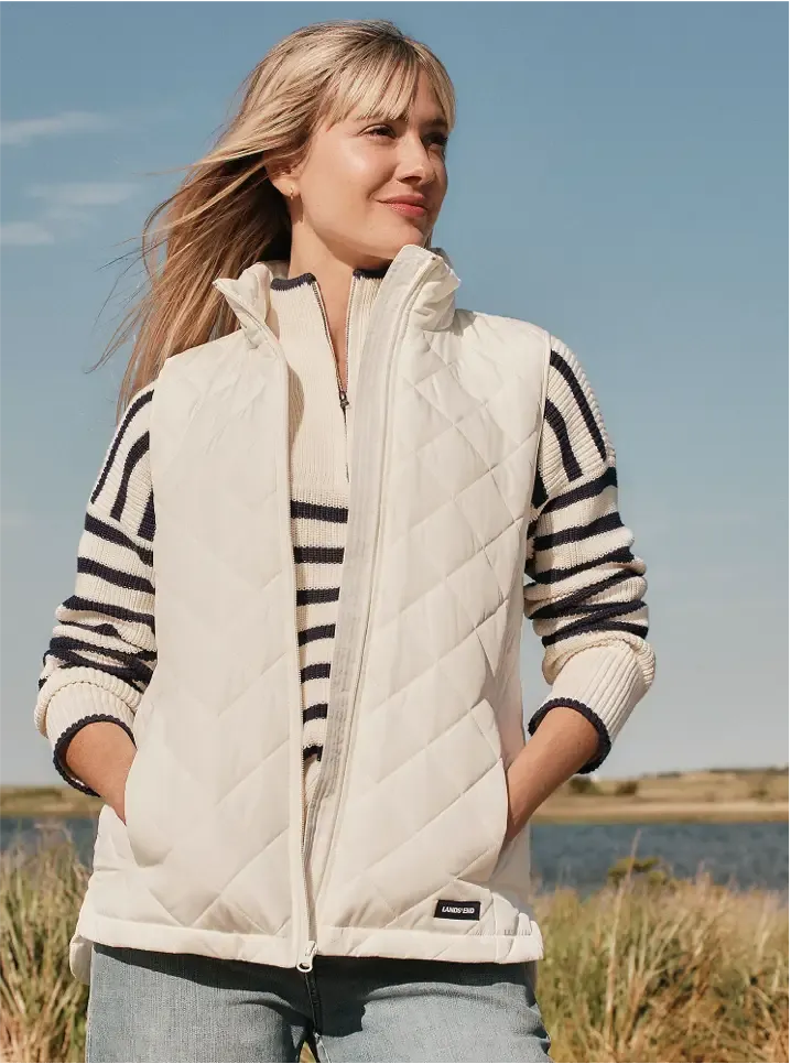 Woman wearing a white quilted zip-up vest over a striped navy-and-cream sweater.