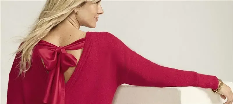 Woman wearing a red sweater dress with red bow, gold bracelets on her wrist.