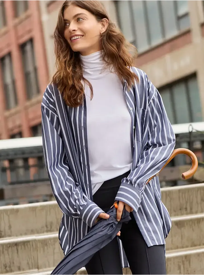Woman wearing a white turtleneck layered under a blue and white striped button-up shirt.