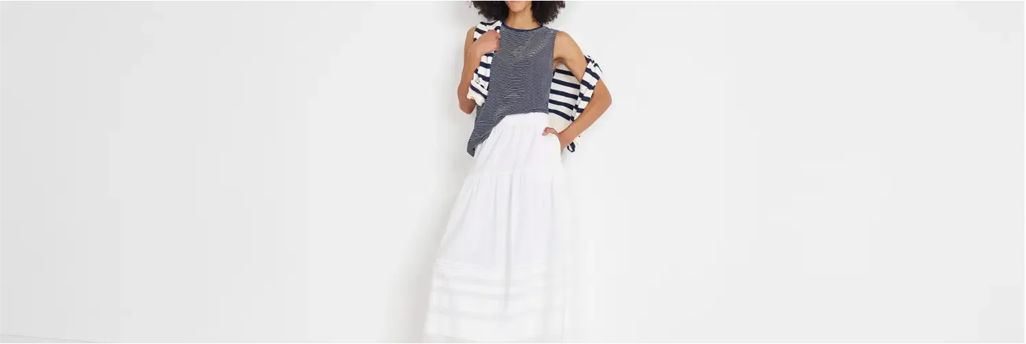 Woman in a navy striped tank top with a light white maxi skirt, draping a striped sweater over her shoulder