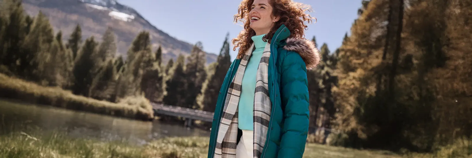 Woman wearing a teal puffer jacket and white and black scarf over a turquoise turtleneck.
